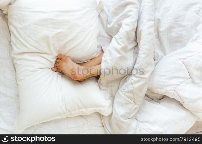 Closeup shot of little girl sleeping upside down and holding feet on pillow