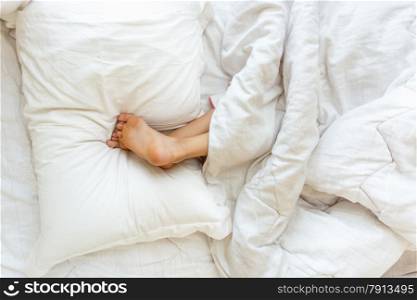 Closeup shot of little girl sleeping upside down and holding feet on pillow