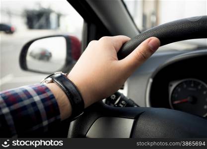 Closeup shot of male hand in watches holding car steering wheel