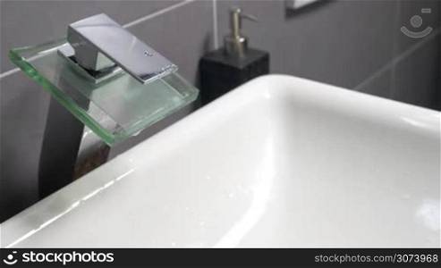 Closeup shot of modern sink tap, undefined person is washing hands with liquid soap under it.