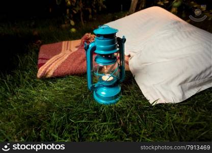 Closeup shot of old oil lamp standing on grass next to pillow and blanket