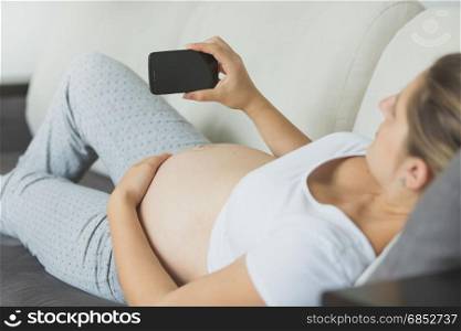 Closeup shot of pregnant woman relaxing on sofa and using mobile phone
