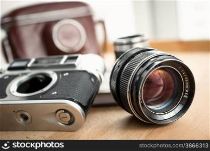 Closeup shot of retro camera, lens and leather case lying on wooden table
