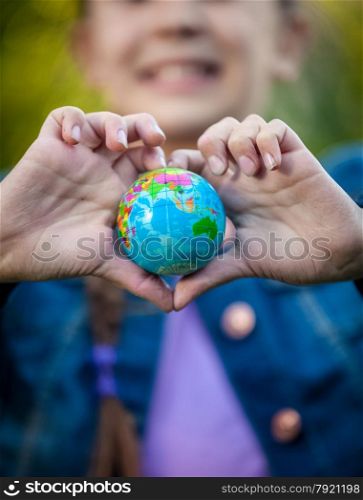 Closeup shot of smiling girl holding globe in hands folded in shape of heart