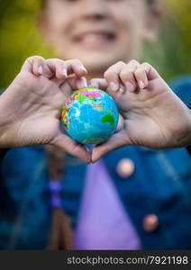 Closeup shot of smiling girl holding globe in hands folded in shape of heart