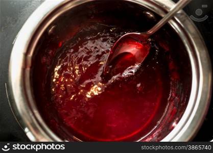 Closeup shot of stirring cherry jam with spoon in metal saucepan