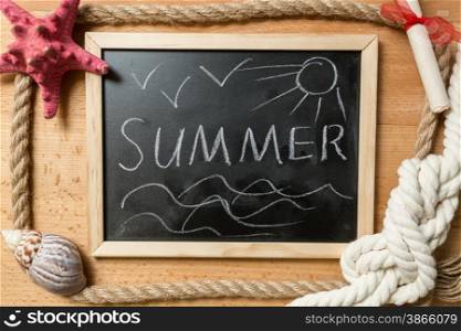 "Closeup shot of "summer" written on blackboard with frame of ropes, seashells and knots"