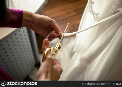 Closeup shot of tailor cutting off ribbon on white wedding dress
