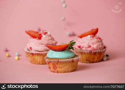Closeup shot of three colorful cupcakes with strawberries on pink background with colorful candies