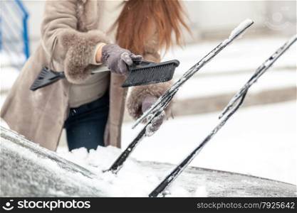 Closeup shot of woman cleaning car wipers from snow with brush