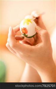 Closeup shot of woman drawing flower on easter egg
