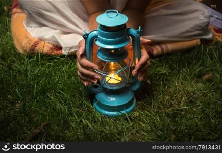 Closeup shot of woman sitting at garden at night and warming hands on lantern