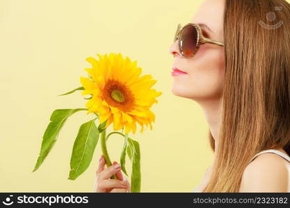 Closeup side view of attractive summer woman in sunglasses with sunflower in her hand on yellow background