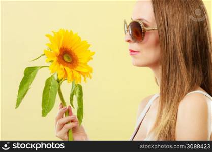 Closeup side view of attractive summer woman in sunglasses with sunflower in her hand on yellow background