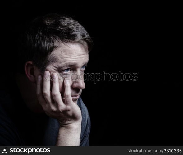 Closeup side view of mature man with his chin in hand displaying depression on black background