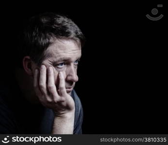 Closeup side view of mature man with his chin in hand displaying depression on black background