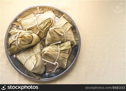 Closeup Sticky rice dumpling or Zongzi on stainless steel tray for Dragon Boat Festival on cream color fabric. Pay respect to ancestor. Copy space wallpaper.