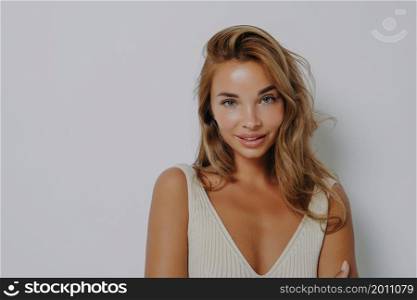 Closeup studio portrait of young beautiful european woman smiling mysteriously and looking at camera slightly bowing her head, isolated over grey wall background with copy space for text. Women beauty. Portrait of young beautiful blonde woman smiling mysteriously at camera, isolated on grey background