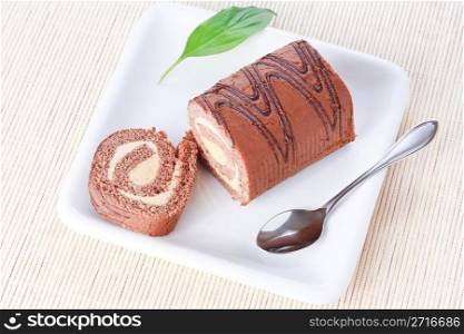Closeup swiss roll with condensed milk cream on a white plate with spoon and a green leaf