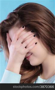 Closeup teenage girl cover the face with her hand. Ashamed confused young woman studio shot on blue
