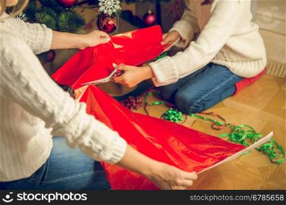 Closeup toned image of girl cutting red wrapping paper for Christmas presents