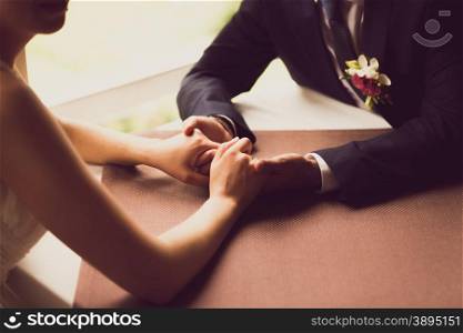 Closeup toned photo of bride and groom holding hands at restaurant