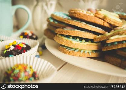 Closeup toned photo of freshly baked cookies and colorful candies on old wooden desk