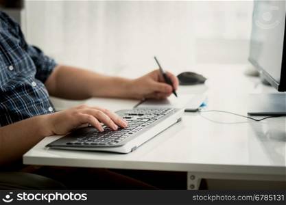 Closeup toned photo of graphic designer using tablet and keyboard at work