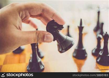 Closeup toned photo of man making move with black horse at chess game