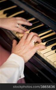 Closeup toned photo of newly married couple playing on piano
