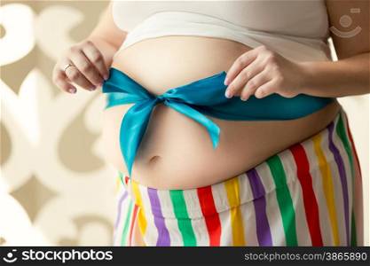 Closeup toned photo of young pregnant woman holding bow on tummy