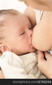 Closeup toned portrait of 3 months old baby boy sucking mothers breast