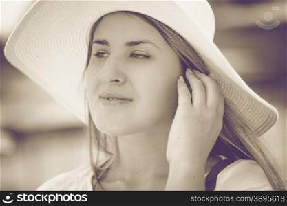 Closeup toned portrait of beautiful woman in white hat posing on beach at windy day
