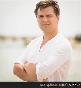 Closeup toned portrait of handsome man in white shirt with hands crossed relaxing on the beach