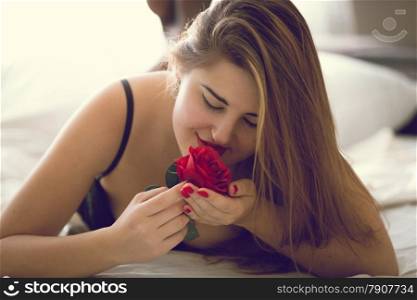 Closeup toned portrait of sexy woman posing with red rose in bed