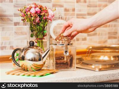 Closeup toned shot of man taking cookies out of glass jar at kitchen