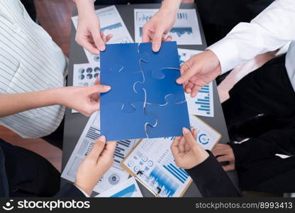 Closeup top view business team of office worker putting jigsaw puzzle together over table filled with financial report paper in workplace with manager to promote harmony concept in meeting room.. Closeup top view business people join jigsaw puzzle together in harmony office