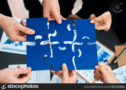 Closeup top view business team of office worker putting jigsaw puzzle together over table filled with financial report paper in workplace with manager to promote harmony concept in meeting room.. Closeup top view business people join jigsaw puzzle together in harmony office
