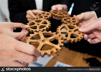 Closeup top view businesspeople hand holding gear and join together over meeting table with financial report papers. Cohesive group of office workers holding cog wheel as synergy harmony concept.. Closeup top view hands holding gears over table with BI reports for harmony.