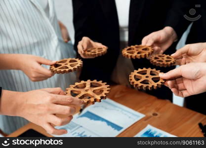 Closeup top view businesspeople hand holding gear and join together over meeting table with financial report papers. Cohesive group of office workers holding cog wheel as synergy harmony concept.. Closeup top view hands holding gears over table with BI reports for harmony.