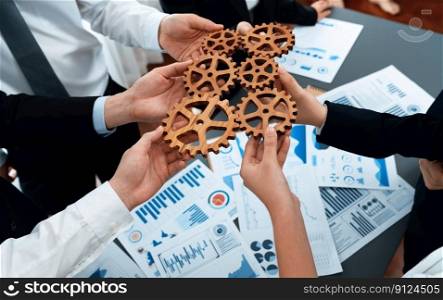 Closeup top view businesspeople hand holding gear and join together over meeting table with financial report papers. Cohesive group of office workers holding cog wheel as synergy harmony concept.. Closeup top view hands holding gears over table with BI reports for harmony.