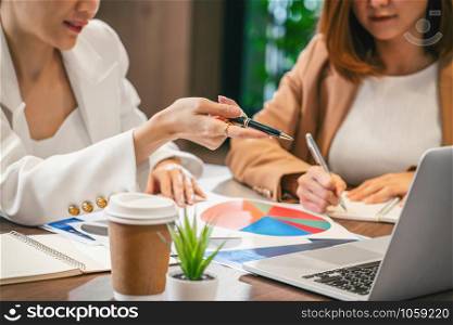 Closeup Two asian businesswomen working with the partner business by point finger to the technology laptop in modern meeting room, office or working space, coffee break, partner and colleague concept