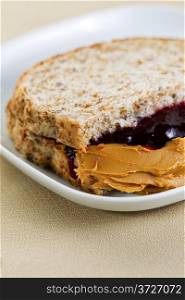 Closeup vertical photo of peanut butter and jelly sandwich, cut in half, inside white plate on textured table cloth underneath