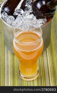Closeup vertical photo of tall glass filled with golden color beer with bottled beer in ice bucket in background