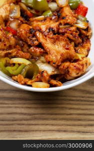 Closeup vertical view of Chinese spicy chicken dish in white bowl with rustic wooden boards underneath