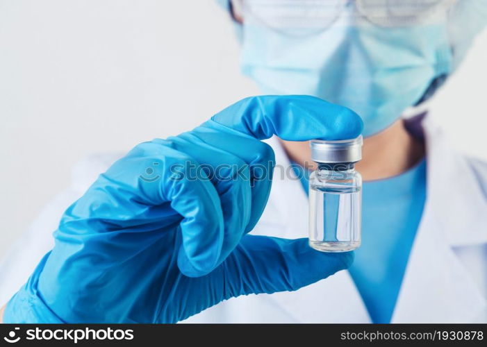 Closeup vial of covid-19 vaccine in hand of professional scientist or doctor in laboratory for treatment with mask gloves and lab coat on white background. Health business and industry concept.