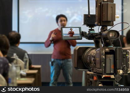 Closeup Video recording the Asian Speaker with casual suit on the stage over the presentation screen in the meeting room of business or education seminar, event and seminar concept