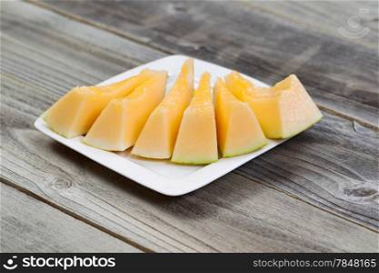 Closeup view of a freshly cut melon slices on white plate on rustic wood