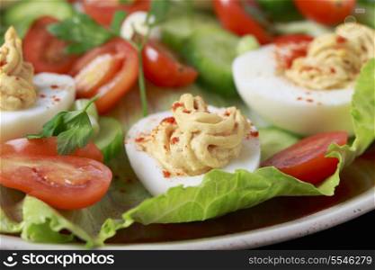 Closeup view of a salad of deviled eggs served with lettuce, miniature tomatoes, sliced cucumber and chopped green onions or scallions