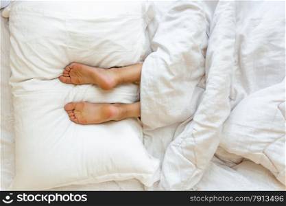 Closeup view of feet lying on soft white pillow at bed